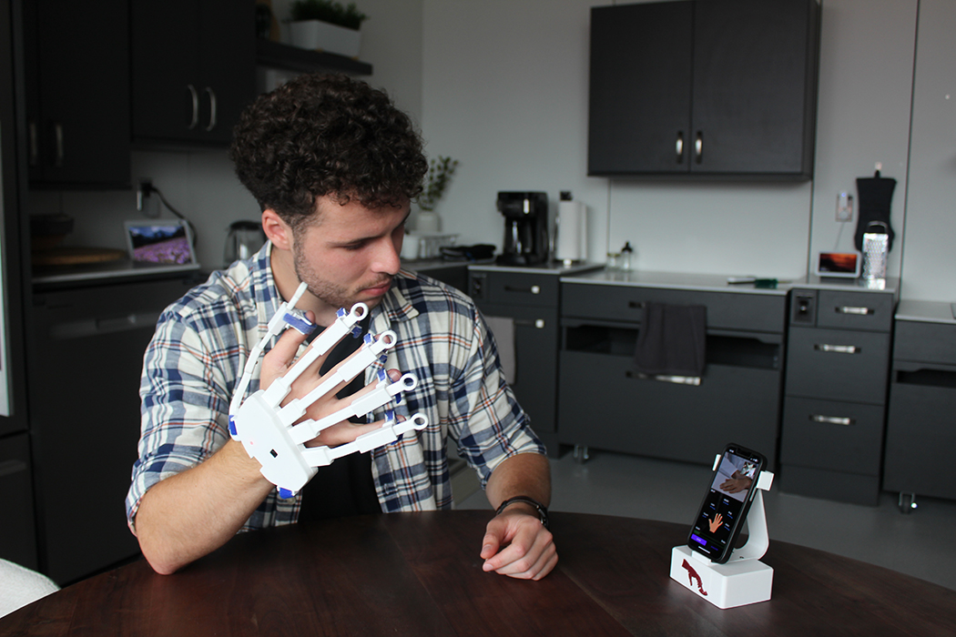 Male student wearing a plastic glove and looking at a smartphone.