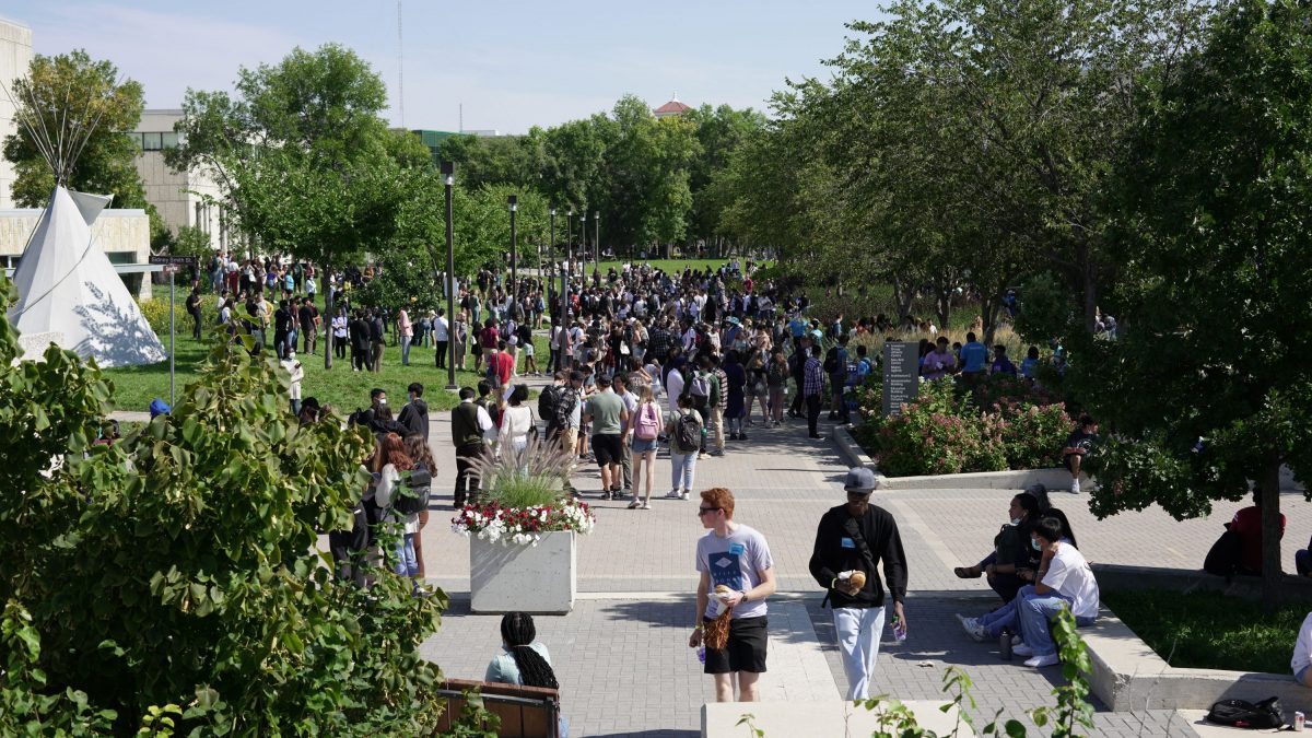 wide shot of um fort garry campus during orientation, many students on curry pedway picutred on sunny day.