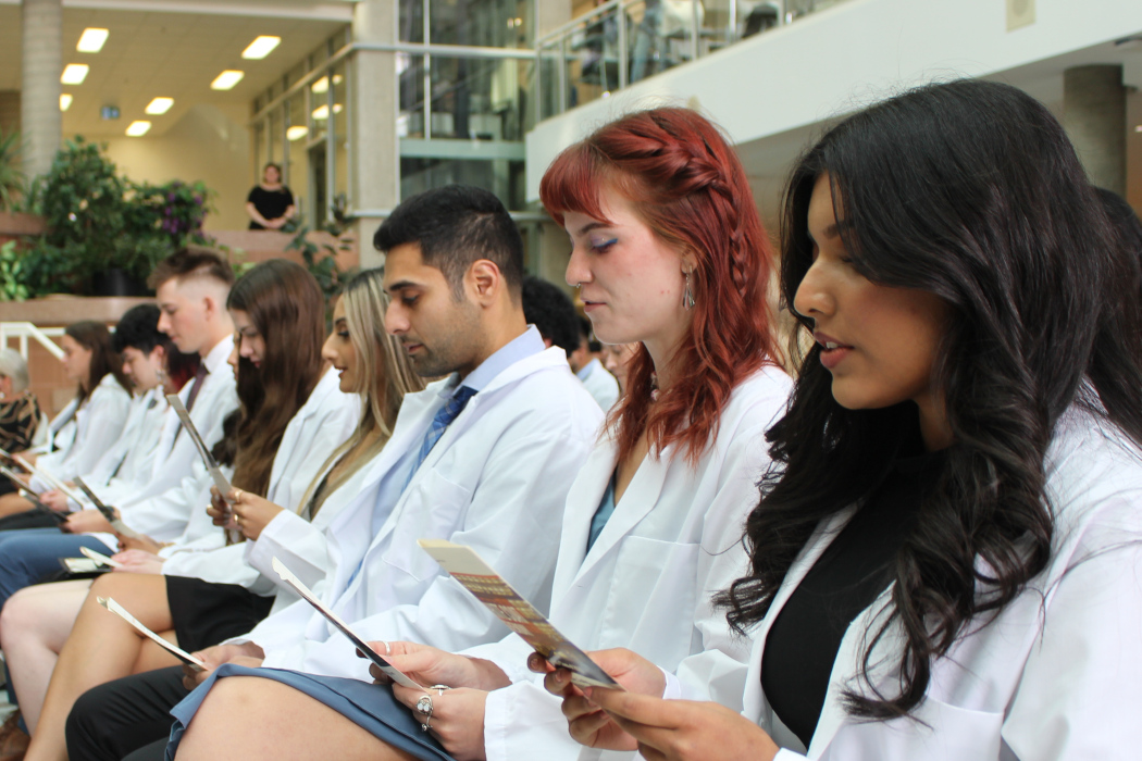 About 10 students wearing white coats read the Pledge of Professionalism off of the programs they are holding.