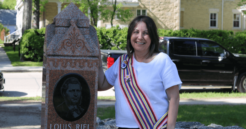 A woman in a Métis sash stands beside a Louis Riel monument.