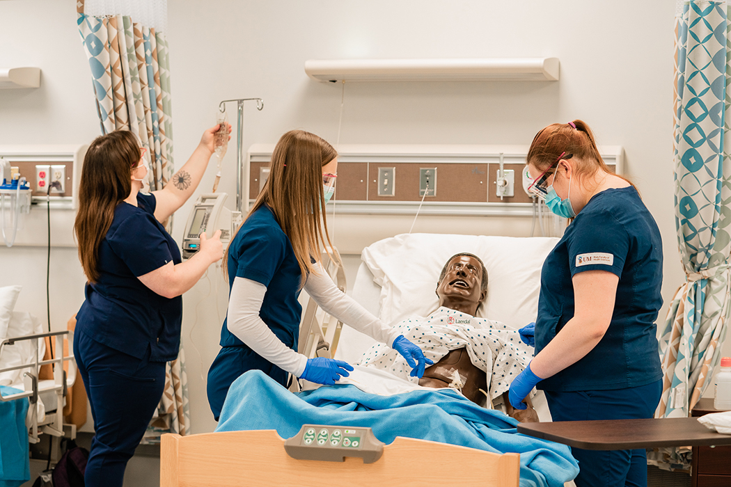 Nursing students working with a manikin in a hospital-style bed in a simulation lab.