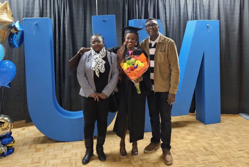 Photo of graduate and her parents by big blue UM letters.