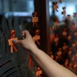 An arm reaches in to place an orange ribbon to a window on Bannatyne campus to honour children lost to residential schools in Manitoba.