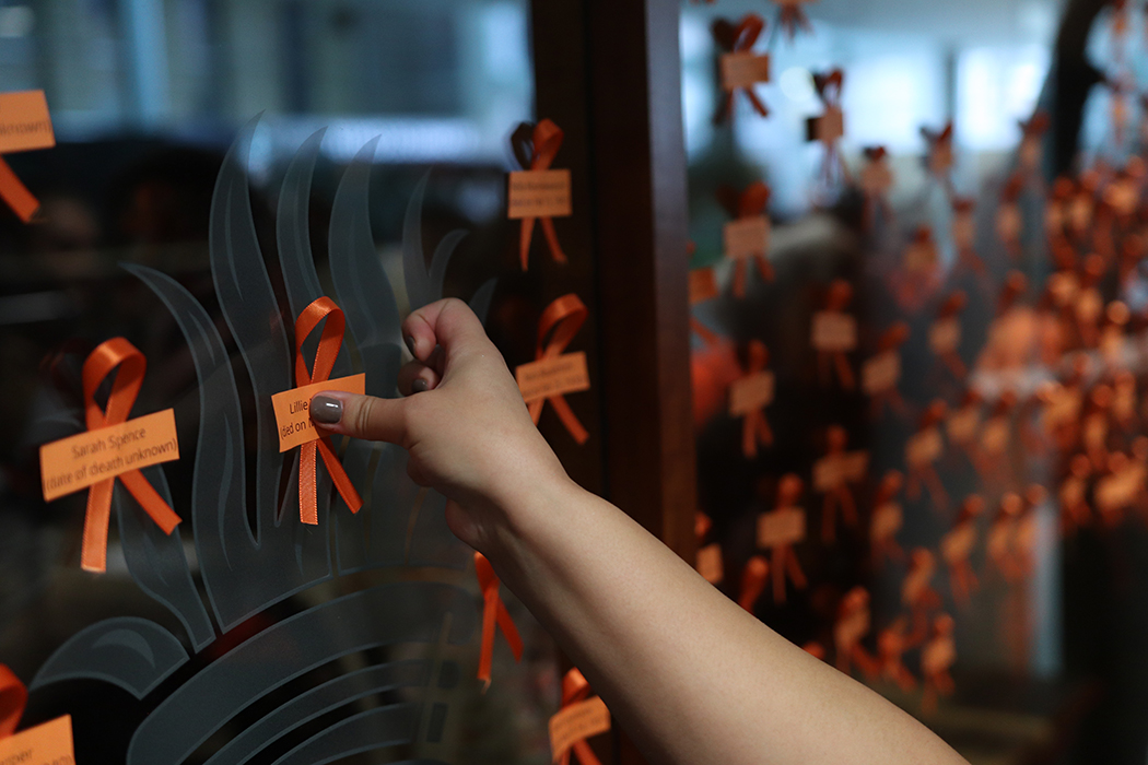 An arm reaches in to place an orange ribbon to a window on Bannatyne campus to honour children lost to residential schools in Manitoba.