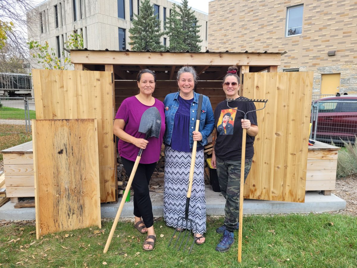 Lodge Caretakers Christine Cyr, Vanessa Lillie and Nicki Ferland stand in front of a wood shed on the Sweat Lodge site behind Migizii Agamik.
