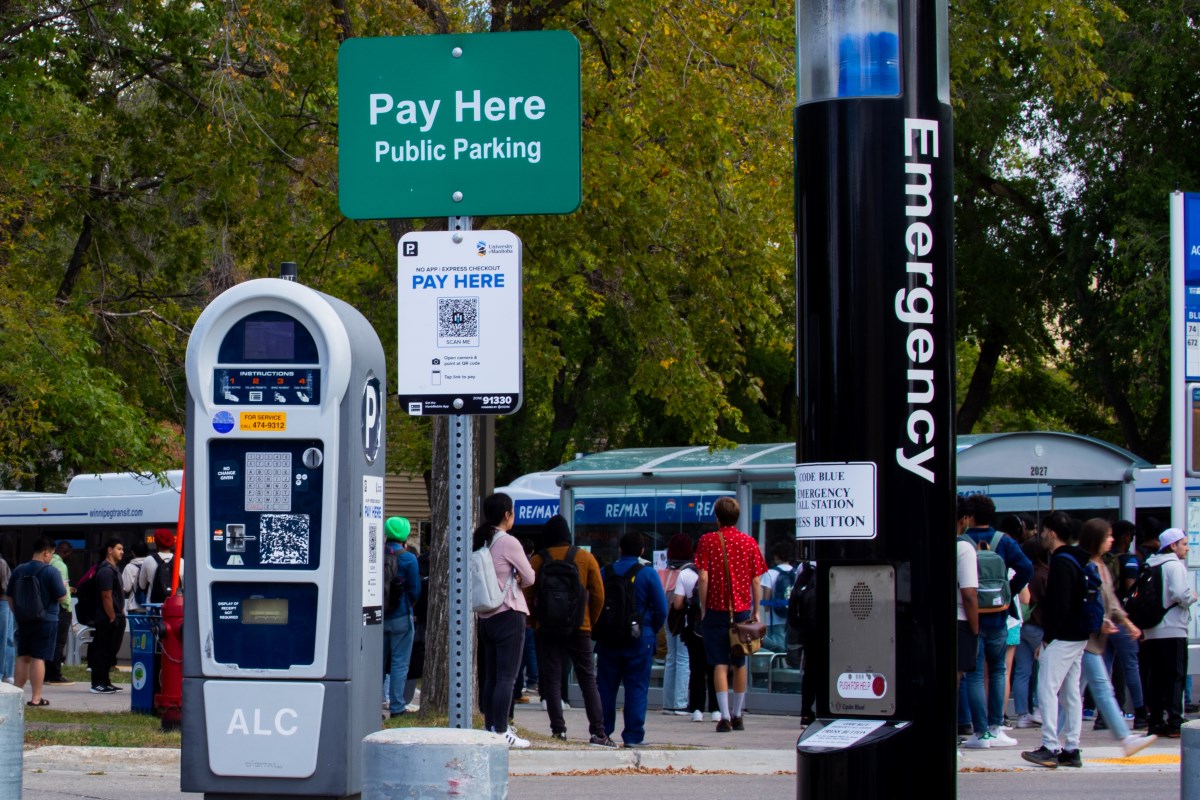 A parking pay station in the foreground, students waiting for transit buses in the background
