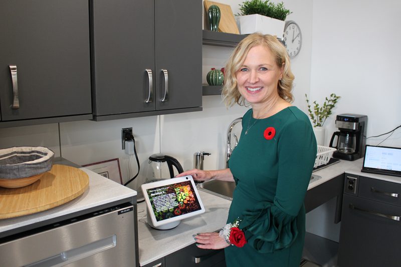 Jacquie Ripat stands at a kitchen counter, operating a touchscreen computer.