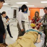 Teens in a hospital simulation lab watch a demonstration with a medical manikin performed by a resident ER doctor.