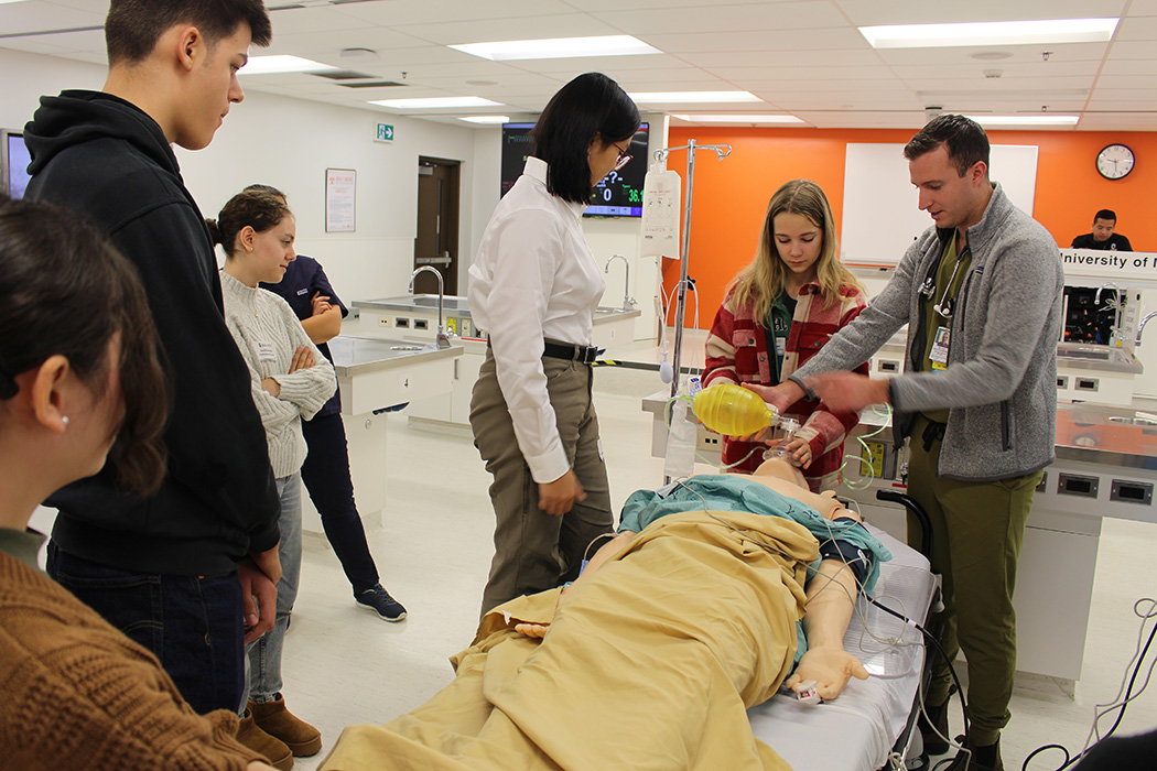 Teens in a hospital simulation lab watch a demonstration with a medical manikin performed by a resident ER doctor.