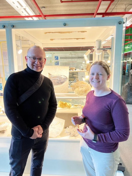 Two people standing in front of a glass display case of fossils.
