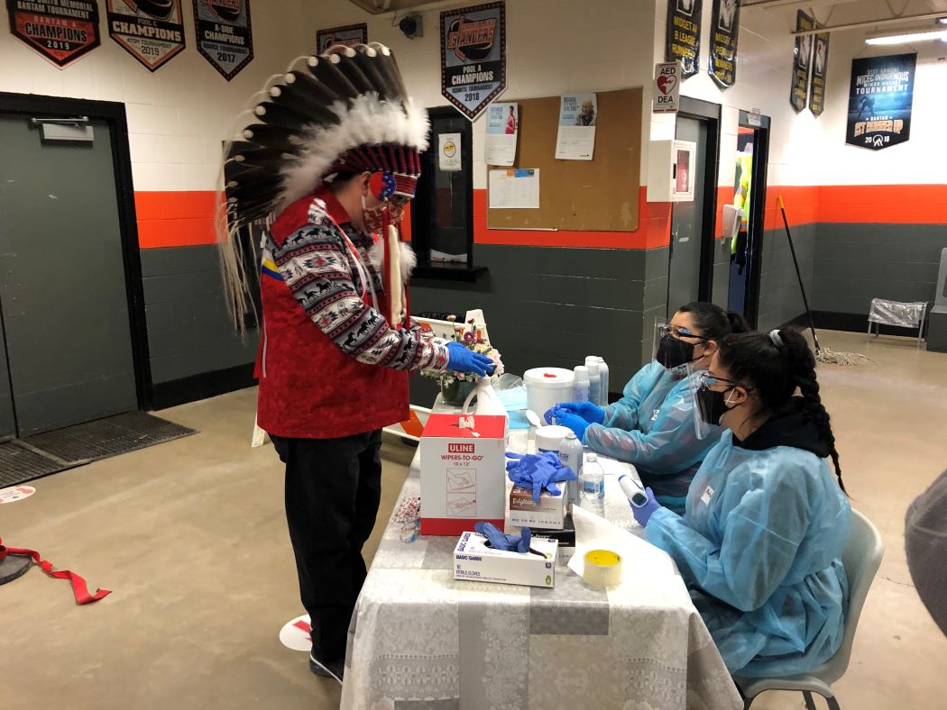 Chief David Monias of Pimicikamak Cree Nation, wearing a headdress, checks in to be vaccinated against COVID-19 in 2021.