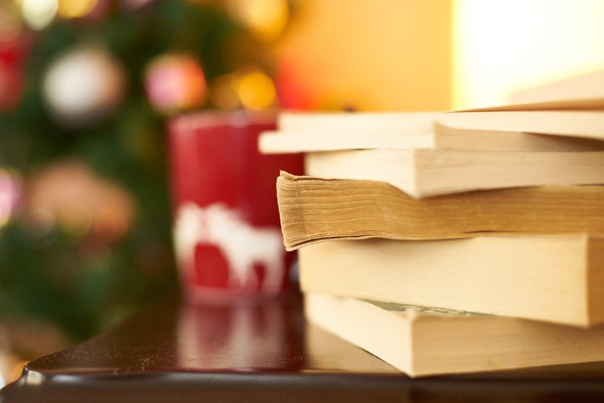 image of books stacked up with mug and holiday lights out of focus.