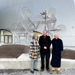 Three people stand in front of a bicycle sculpture made of 18 bicycles. The Desautels Concert Hall is in the background.
