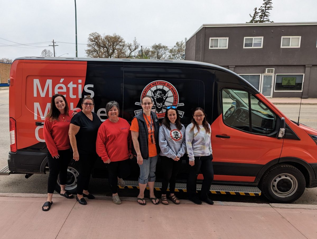Six health-care workers stand in front of a Manitoba Metis Federation van.