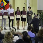 Five students stand in a line with Dr. Kelekis-Cholakis on a stage. A photographer is taking their photo. The students are holding certificates.