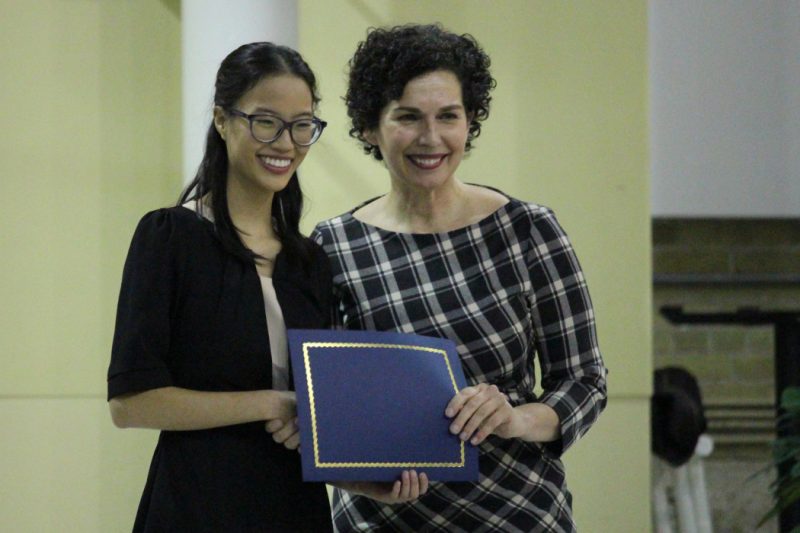 Sophie and Dr. Kelekis-Cholakis pose for a photo. Dr. Kelekis-Cholakis is handing Sophie a folder that holds a certificate. 