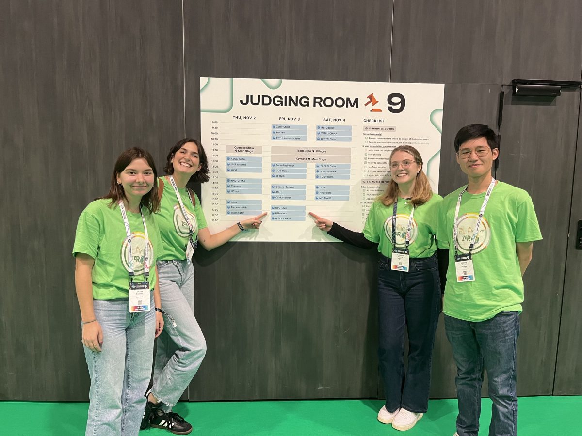 Jessica Marinelli and Camille Prefontaine wearing bright green shirts in the left, with one pointing to the poster behind them, Oleksandra Havruk and Louis Cheng on the right wearing bright green shirts with one pointing to the poster behind them. The poster is on a wall with dark wooden panels.