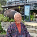 Image of James Kinoshita in front of his home with plants and a stone patio in the background.