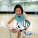 Sandra Webber leans over a pickleball net, holding a racquet.