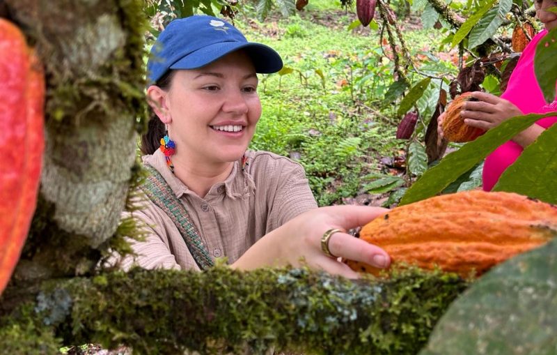 A young woman picking a cacao pod from a plant in rainforest setting.