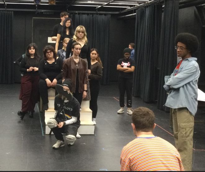 Group of students in a theatre rehearsal space, holding scripts.