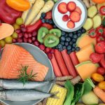 Healthy foods, including carrots, strawberries, red pepper, kiwi, blue berries, tomatoes, melon, salmon, avocado, olives and corn.