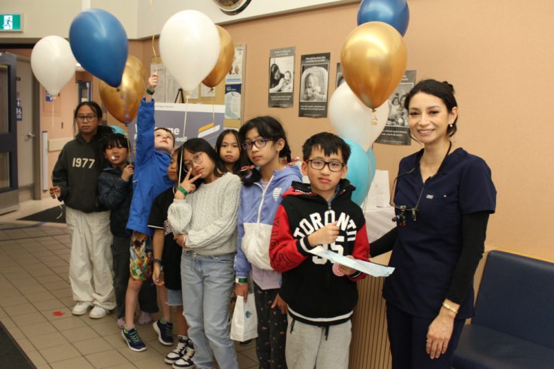 Eight kids pose for the photo holding helium-filled balloons. A dental student stands with them.