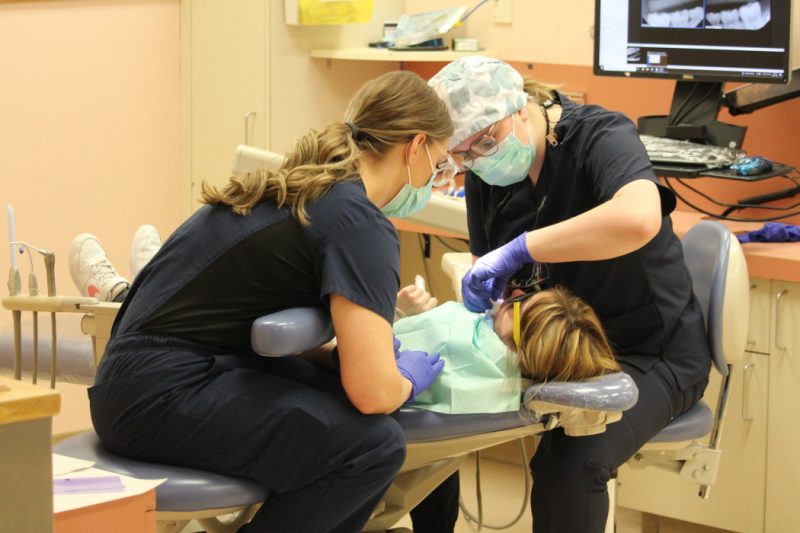 Two dental students treat a child lying in a dental chair.