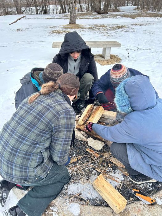 A group of people in winter jackets building a fire outdoors.