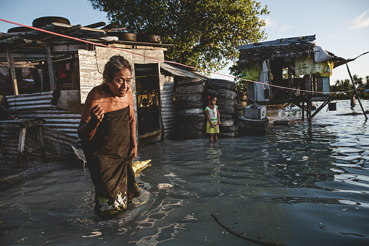 An elderly woman wades through knee-high sea water that flooded her house and village in Kiribati. Each year, the sea level rises by about half an inch // Photo by Jonas Gratzer / Getty Images