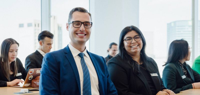 Photo of students smiling in a room, wearing suits. This was from the cover of the Desautels Centre 2024 Impact Report. Photo by 47 Filmworks.