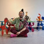 Artist and MFA student Takashi Iwasaki sits cross-legged on the floor surrounded by his art pieces. Photo by Phil Koch.