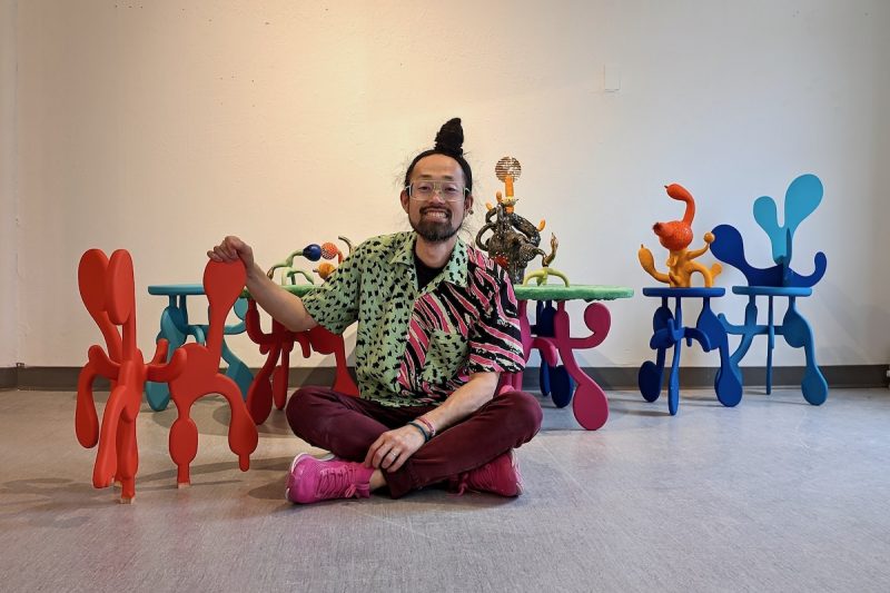Artist and MFA student Takashi Iwasaki sits cross-legged on the floor surrounded by his art pieces. Photo by Phil Koch.