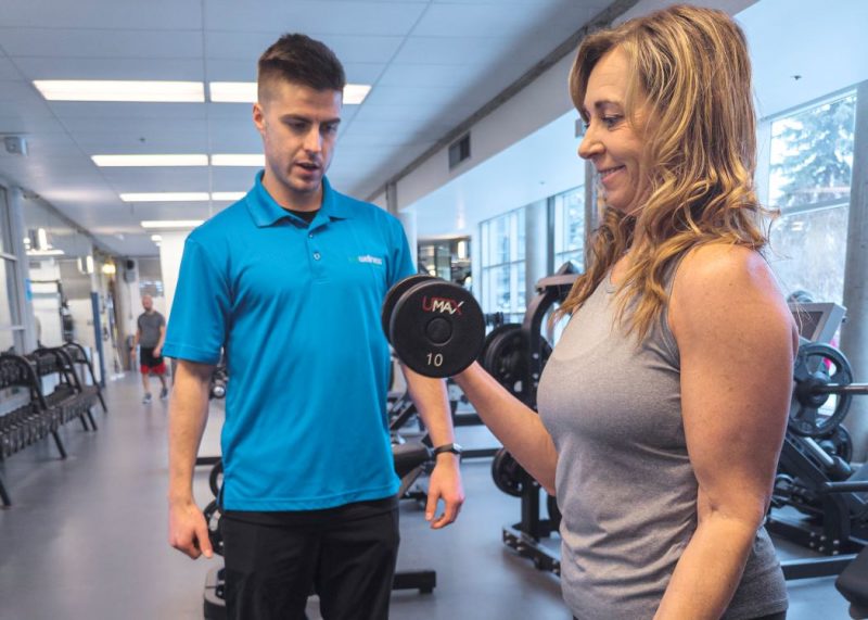A member of the Wellness Institute lifts a dumbbell while a personal trainer supervises.
