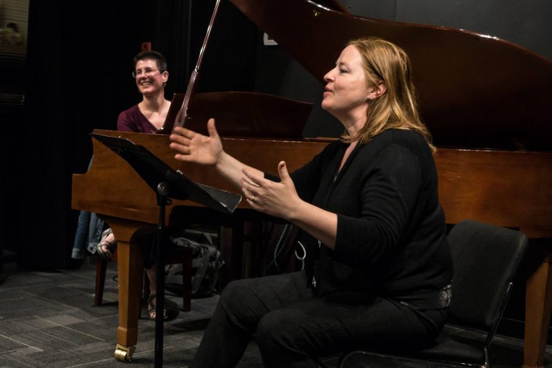 Alison d'amato on the left plays the piano while smiling and Lynne sings on the right