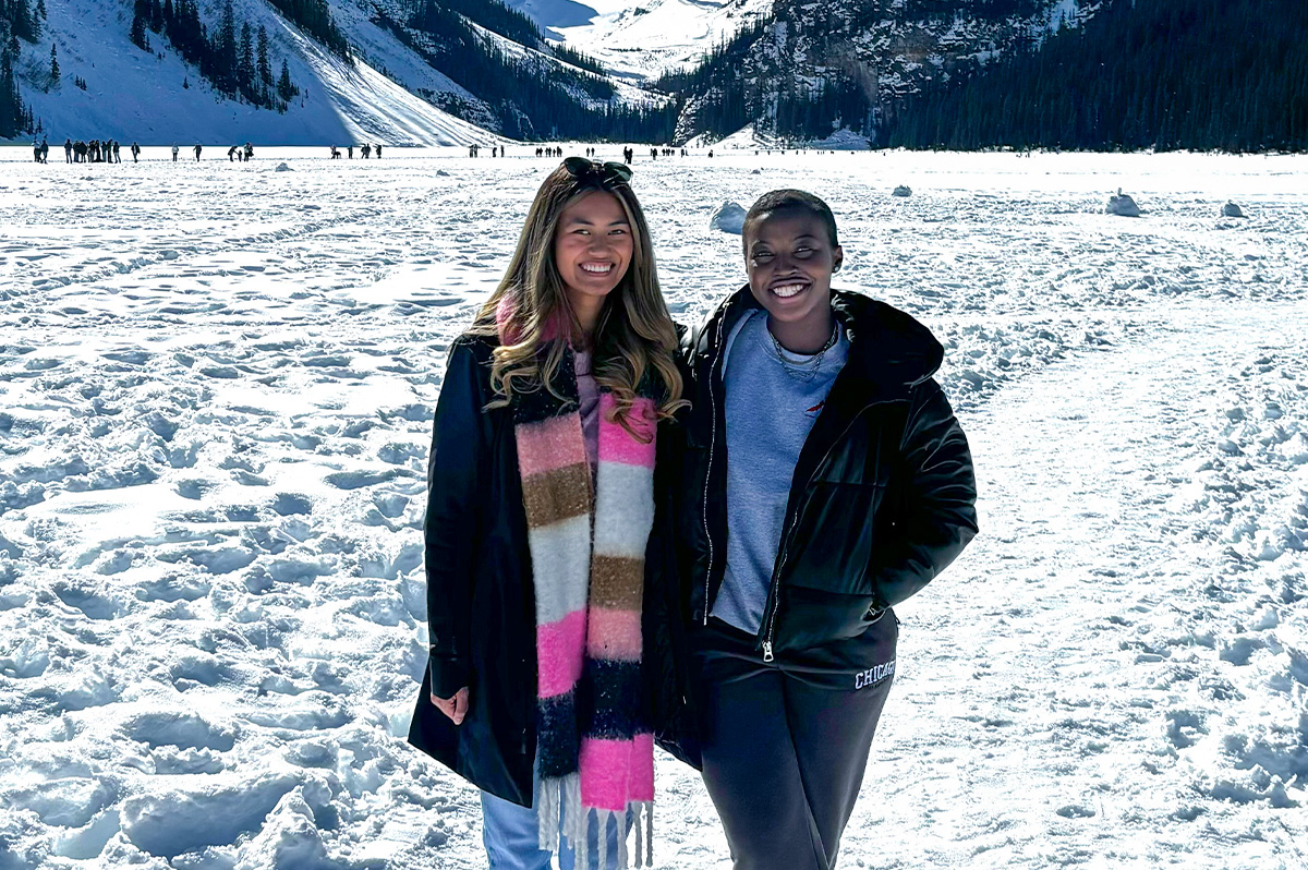 Two women in winter gear standing on a glacier smiling at the camera.