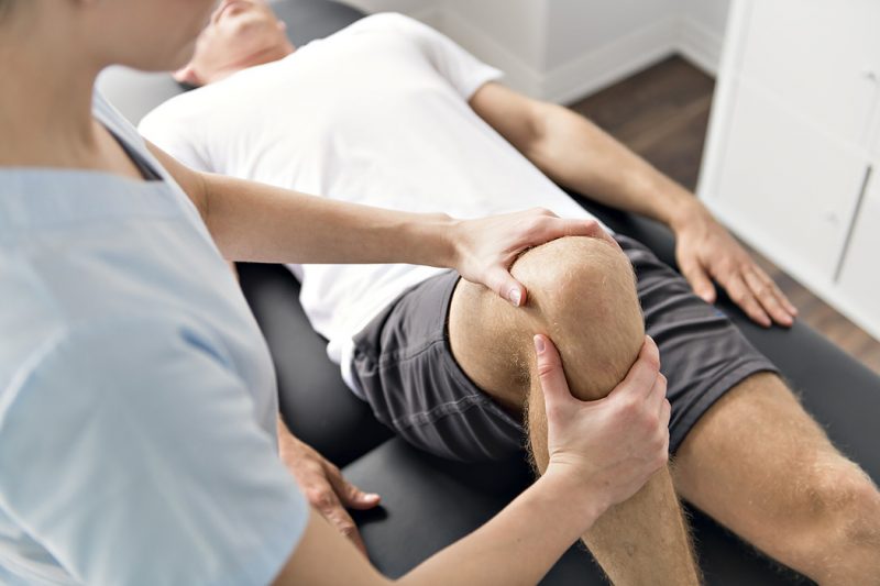 A physiotherapist doing physical exercises with a patient's leg.