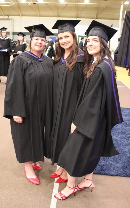 Three female graduates in caps and gowns, wearing red shoes.