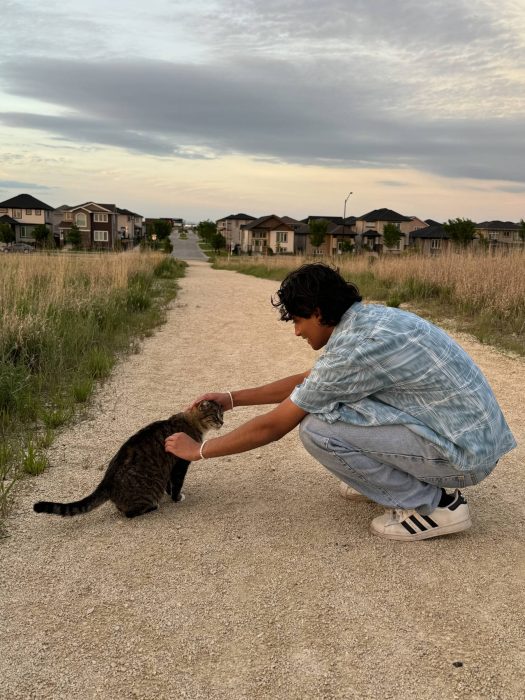 A person crouching outside petting a cat