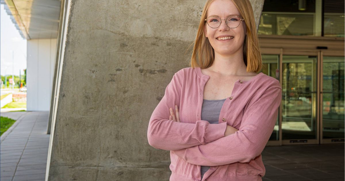 Female wearing glasses standing with arms crossed against a backdrop of a cement wall.