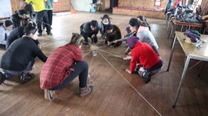 Group people doing an experiential learning exercise, crouching down pulling string from a central object