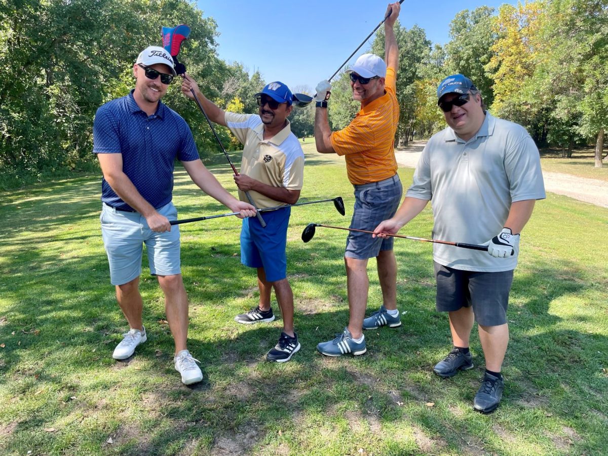 Four people posing with golf clubs on a golfcourse.