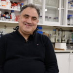 Mazdak Khajehpour, wearing a black shirt, sitting in a chemistry lab, smiling at the camera.