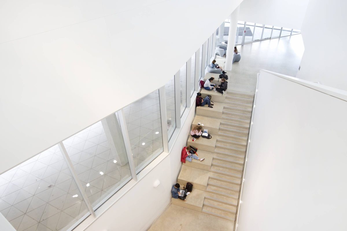 Arial view of students studying alongside a staircase. The building, ARTlab, is has stark white walls, wide windows and limestone floors.