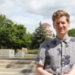 Adam Brandt standing outside at Fort Garry campus. the UM Administration Building can be seen in the background.