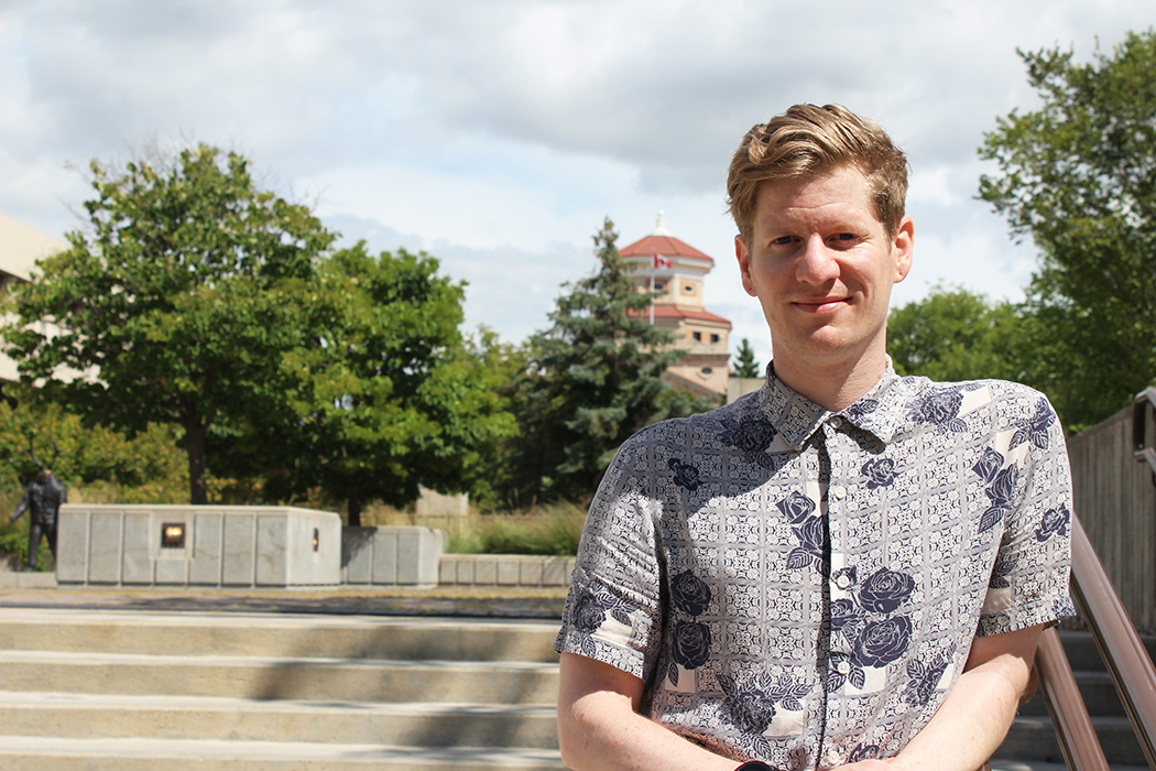 Adam Brandt standing outside at Fort Garry campus. the UM Administration Building can be seen in the background.