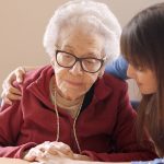 Granddaughter cheers up and hugs her sad grandmother in a nursing home.