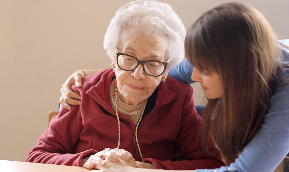 Granddaughter cheers up and hugs her sad grandmother in a nursing home.