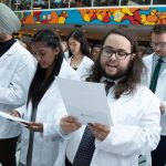 Students wearing white coats stand while reciting the Physician's Pledge.