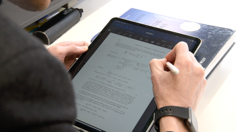 A hand with a digital pen solving a math problem on an iPad .